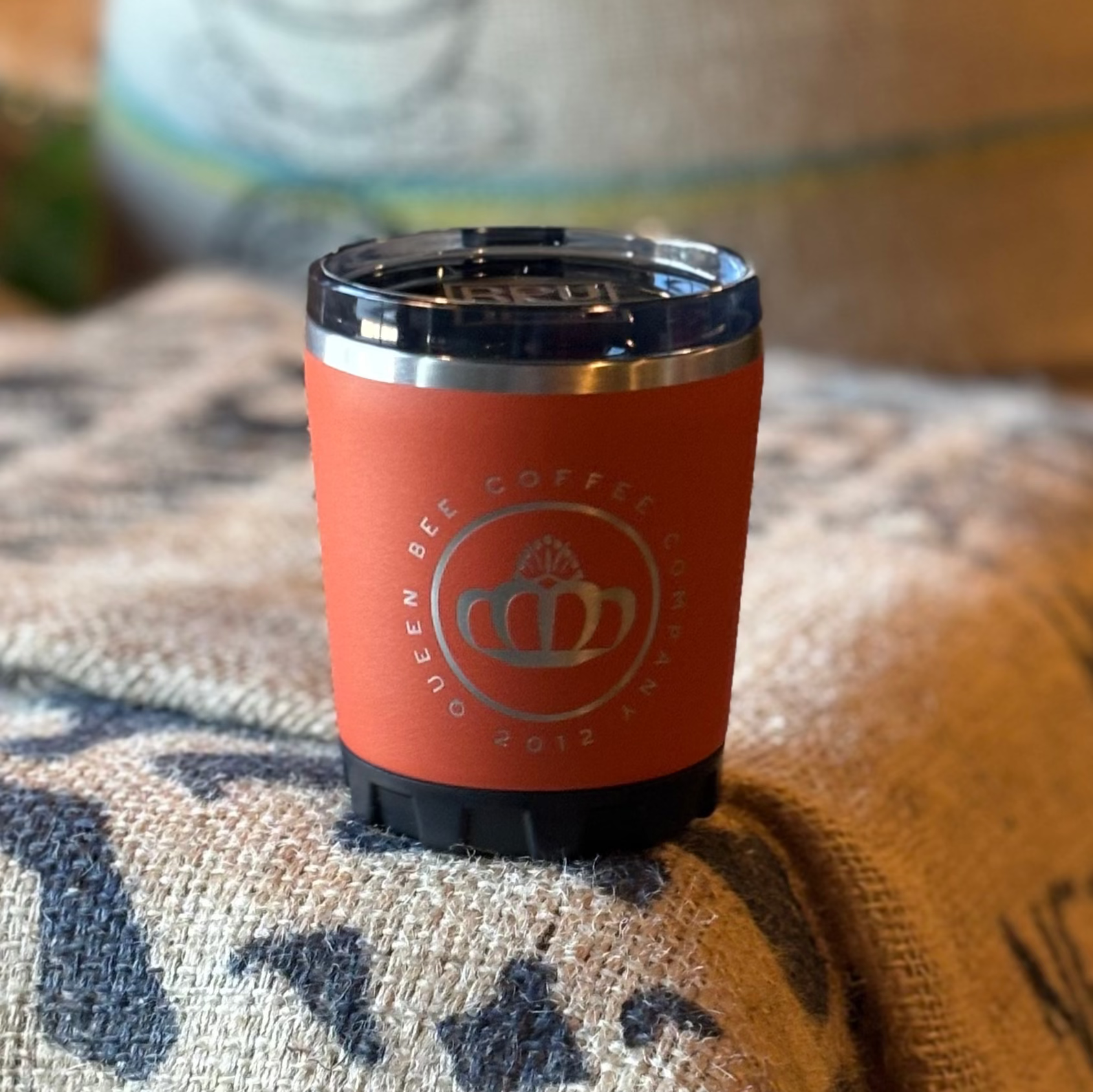 Red coffee tumbler with a logo on a burlap bag