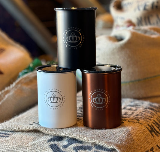 Three metal tumblers in black, white, and bronze on a textured surface with a blurred background.