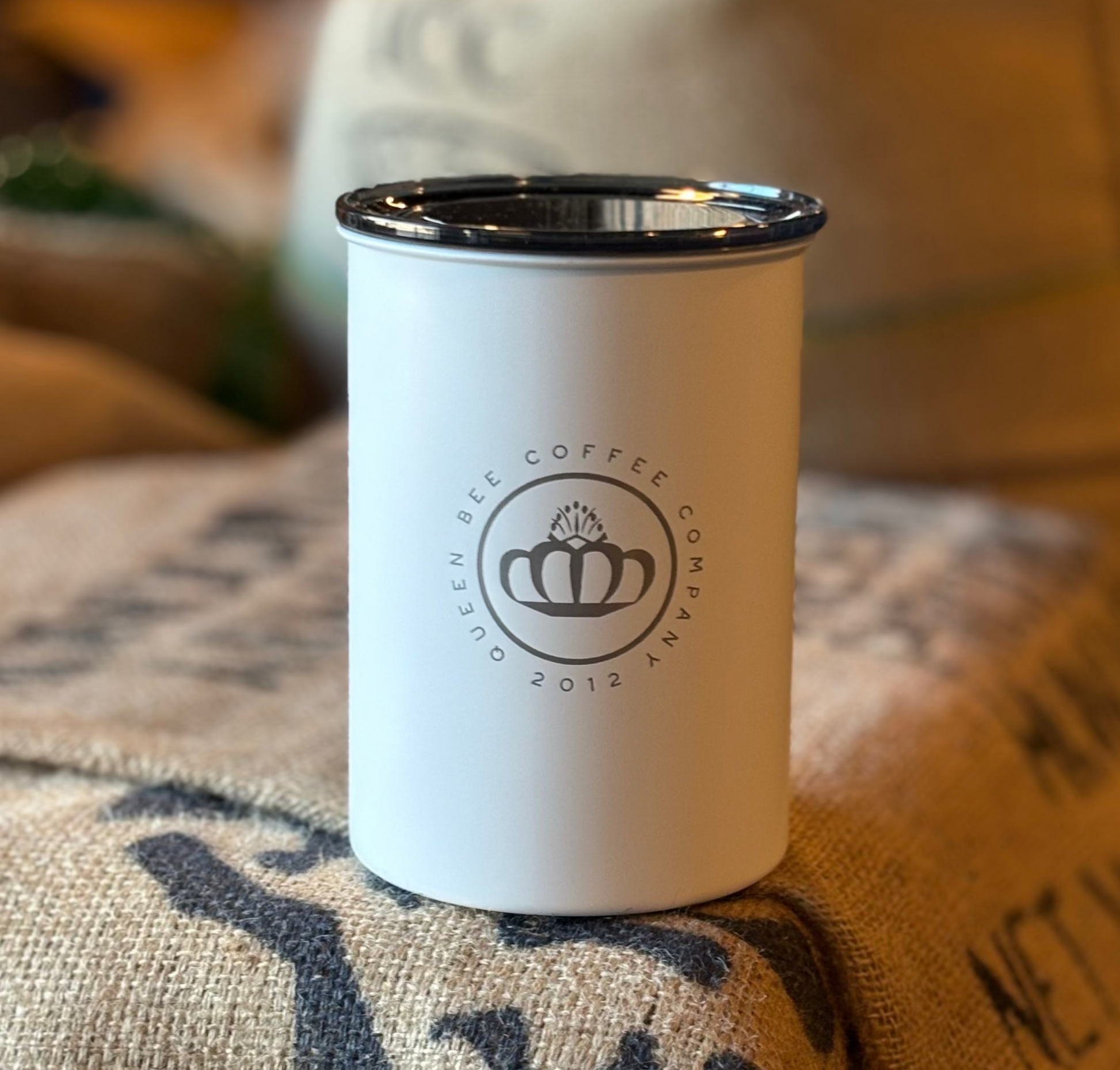 White coffee cup with black rim on a burlap surface, featuring a logo.